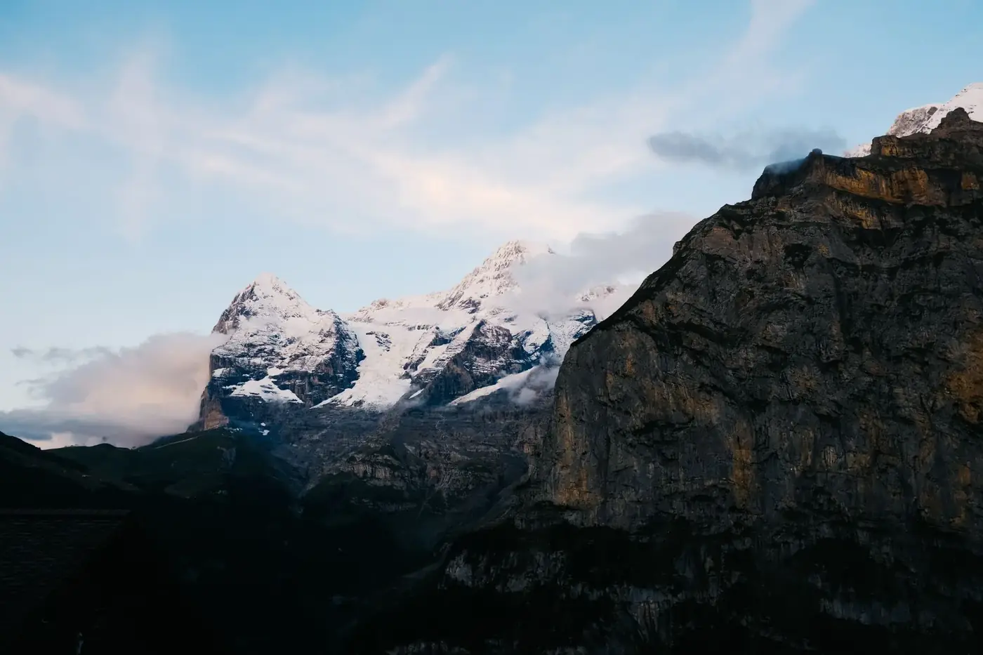 Dramatic view of snowcapped mountain peaks under a blue sky at sunrise, showcasing nature's beauty.