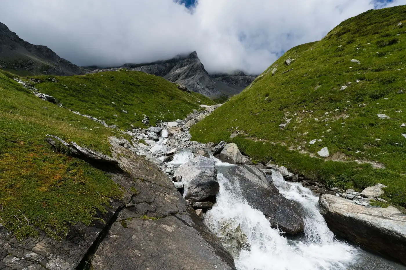 Scenic view of a mountain stream flowing through the Swiss Alps, surrounded by lush green hills.