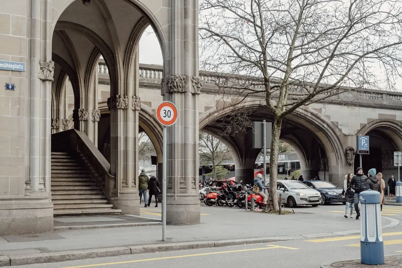 Street view in Zürich's Mühleplatz showcasing Gothic arches and urban life.