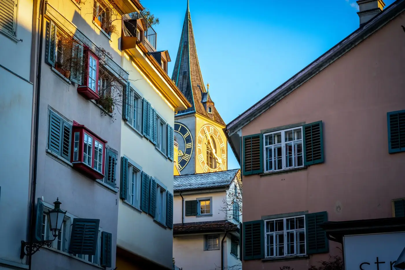Charming view of St. Peter's Church clock tower framed by traditional Swiss architecture in Zurich.