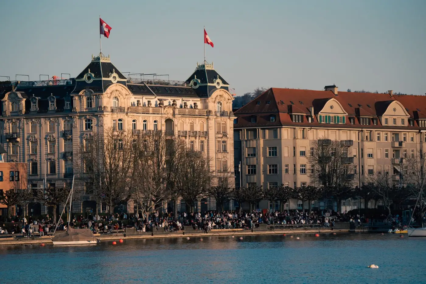 A bustling day by the Zurich waterfront with historic architecture and Swiss flags.