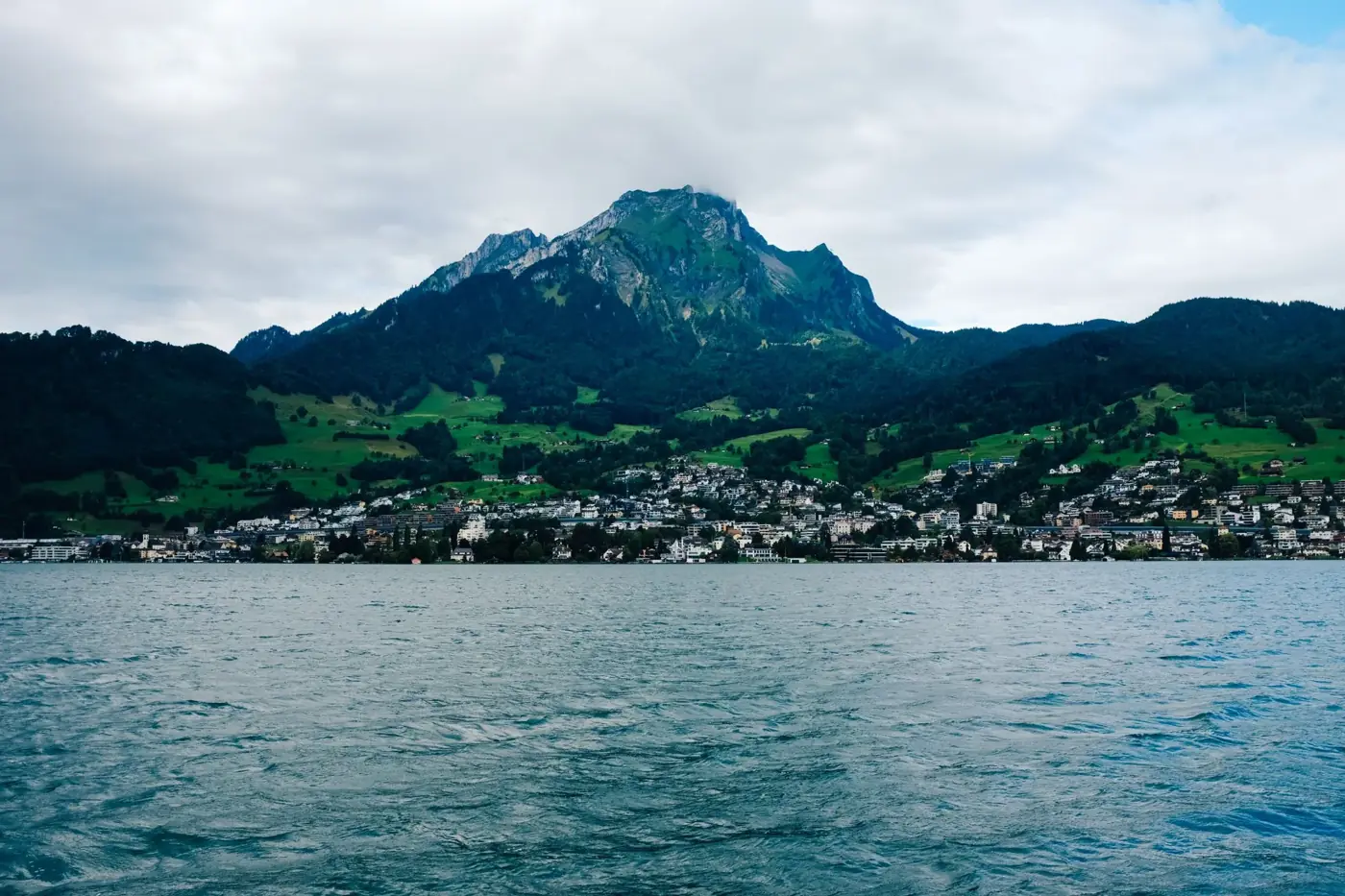 Picturesque lakeside town with majestic mountain backdrop under cloudy sky.