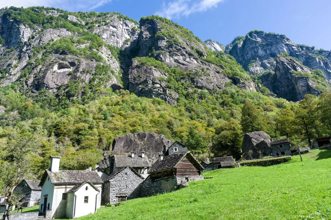 Charming stone houses nestled in a lush Swiss valley surrounded by towering cliffs.