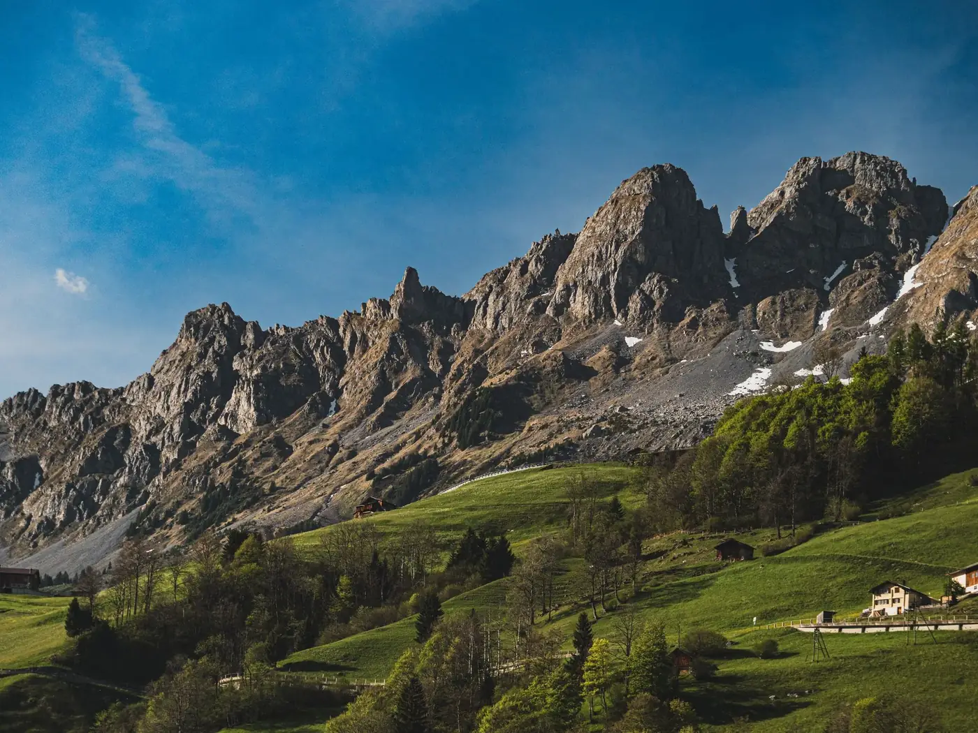 Breathtaking view of the rugged Alps and lush meadows in Unterschächen, Uri, Switzerland, under a clear blue sky.