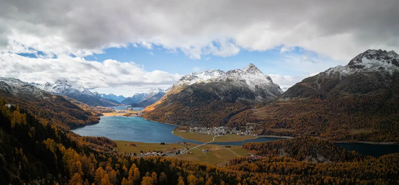 Breathtaking aerial view of the snow-capped Graubünden Alps and colorful autumn forests.